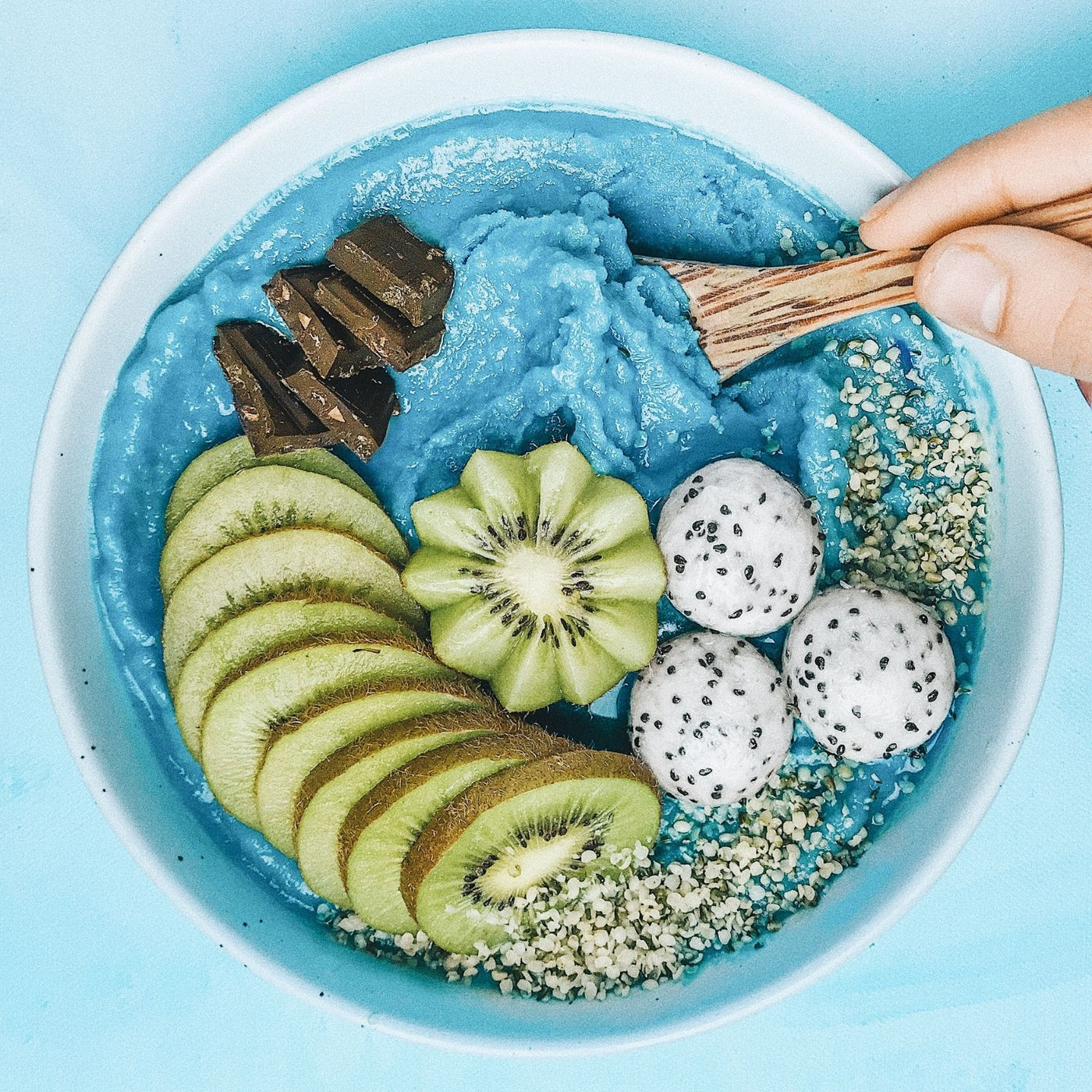 Blue smoothie bowl with kiwi slices, dragon fruit, and chocolate on a light blue background